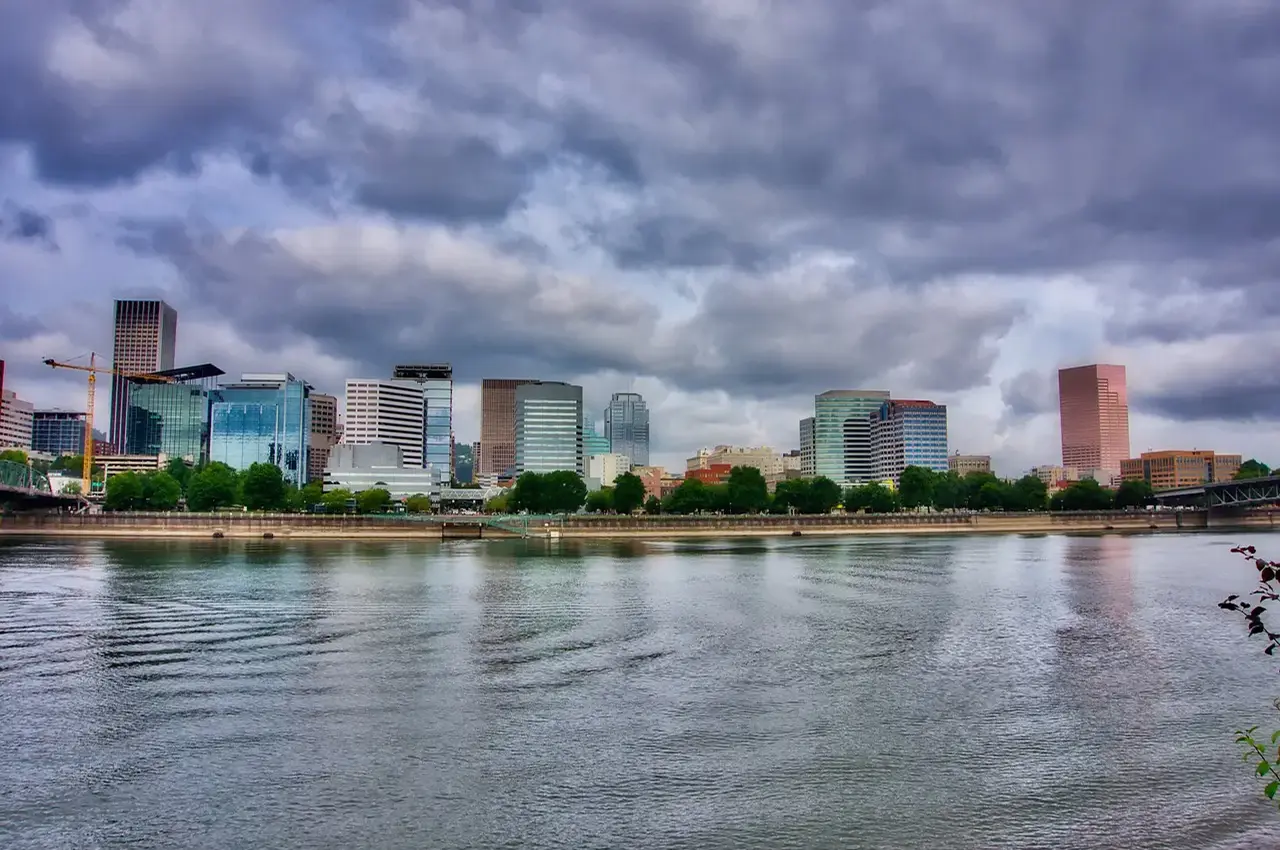 City skyline with cloudy sky reflected on calm water.